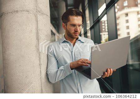 Focused male sales manager in eyeglasses working on laptop standing in office during working day 106364212