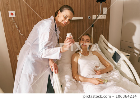 Female doctor showing pills to woman patient in hospital ward during treatment 106364214