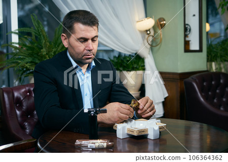 Man cutting cigar before smoking while sitting in a restaurant Man cutting cigar before smoking while sitting in a restaurant 106364362
