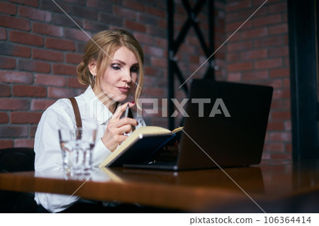 Beautiful senior woman working in cafe with laptop and writing in notepad Beautiful senior woman working in cafe with laptop and writing in notepad 106364414