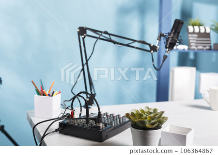 Sound controller console and professional microphone on table at empty blogger workspace. Audio mixer professional equipment on desk in vlogger home studio with no people 106364867