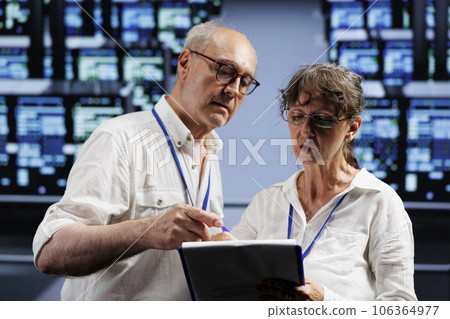 Elderly computer scientists monitoring data center racks, optimizing them for data processing requirements of AI applications. Supervisors oversee neural network server farm used for machine learning 106364977