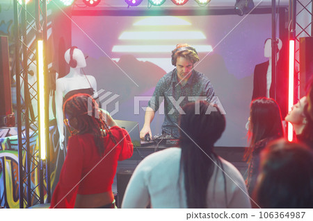 Man dj performing using electronic music mixer and laptop on stage in nightclub. Musician in headphones playing at concert in dark club with spotlights at discotheque party 106364987