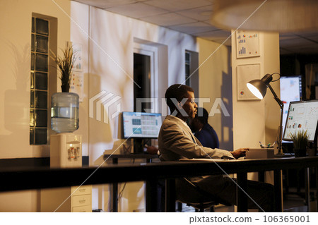Entrepreneur analyzing company statistics working at financial growth report late at night in startup office. African american manager planning marketing strategy to increase business profit Entrepreneur analyzing company statistics working at financial growth report late at night in startup office. African american manager planning marketing strategy to increase business profit 106365001