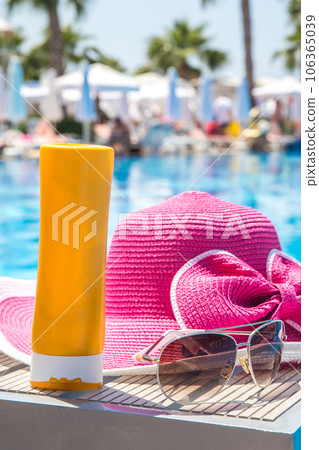 Bottle of sun cream, hat and sunglasses next to swimming pool in hotel Bottle of sun cream, hat and sunglasses next to swimming pool in hotel 106365039