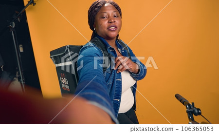 POV of african american delivery person holding mobile phone and doing online conference vlog for remote conversation. Youthful black woman on bicycle conversing about courier service job. POV of african american delivery person holding mobile phone and doing online conference vlog for remote conversation. Youthful black woman on bicycle conversing about courier service job. 106365053