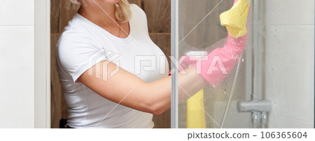 Young woman cleaning glass shower cabin with sponge and spray bottle Young woman cleaning glass shower cabin with sponge and spray bottle 106365604