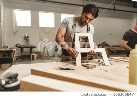 Young man carpenter wearing uniform working in joinery making wooden furniture 106366647