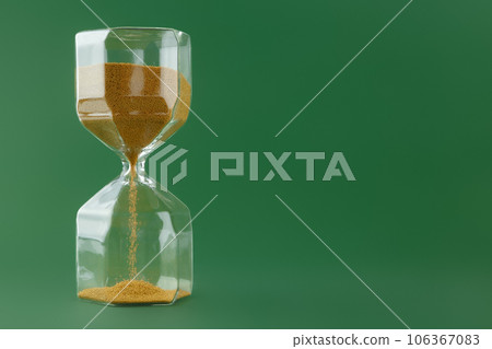 Gold hourglass on dark green paper background Gold hourglass on dark green paper background 106367083