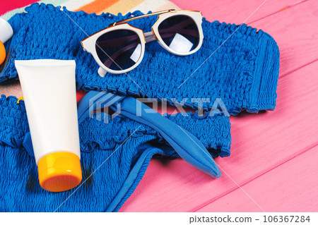 Blue bikini with sunblock cream bottle on bright pink wooden background 106367284