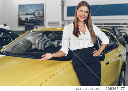 Attractive young female car dealer standing in showroom Attractive young female car dealer standing in showroom 106367477