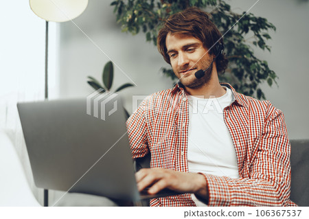 Young man wearing headset doing a video call by laptop 106367537