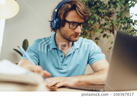 Young man in blue shirt sits at the table and studies with laptop Young man in blue shirt sits at the table and studies with laptop 106367817