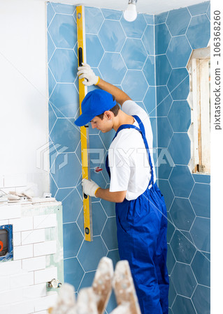 Male builder in blue overalls measures deviations from a given vertical wall using building level 106368260
