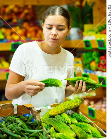Dissatisfied young female customer buying bitter gourd in shop Dissatisfied young female customer buying bitter gourd in shop 106368302