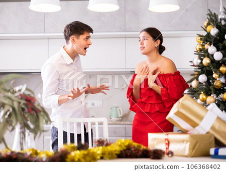Furious young European man and woman in red dress yelling at each other during preparations for New Year in cuisine Furious young European man and woman in red dress yelling at each other during preparations for New Year in cuisine 106368402