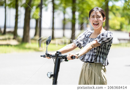 年輕可愛的女人在閃亮的陽光和綠樹下用電動踢腳板清爽地奔跑 | 電動踢腳板圖片 106368414