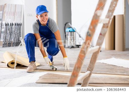 Professional female builder laying laminate flooring in room being renovated Professional female builder laying laminate flooring in room being renovated 106368443