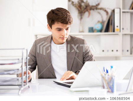 Young man office manager sitting at table and using laptop computer 106368504