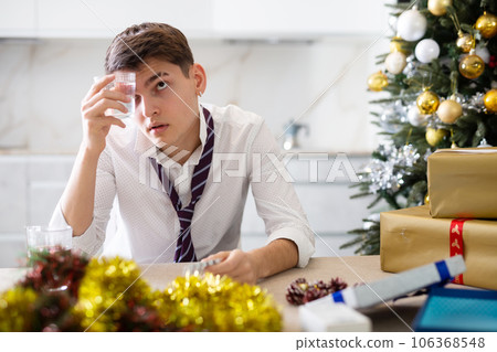 Young lonely man drinking alcohol at christmas table at home Young lonely man drinking alcohol at christmas table at home 106368548