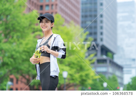 Young woman taking a break and drinking water while jogging in the city Young woman taking a break and drinking water while jogging in the city 106368578