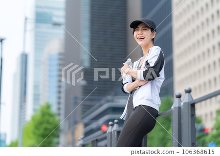 Young woman taking a break and drinking water while jogging in the city 106368615