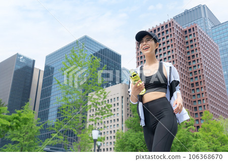 Young woman taking a break and drinking water while jogging in the city 106368670
