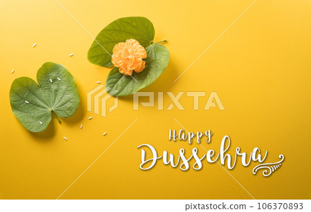 Happy Dussehra. Yellow flowers, green leaf, rice and the text on yellow paper background. Dussehra Indian Festival concept. Happy Dussehra. Yellow flowers, green leaf, rice and the text on yellow paper background. Dussehra Indian Festival concept. 106370893