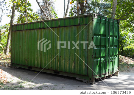 Green cargo container stands in shadow of trees 106373439