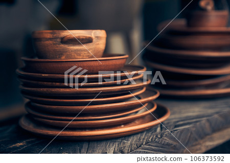 A stack of clay plates of different sizes on a dark background. Level position, top view. Brown plates are on a wooden shelf. High quality photo 106373592