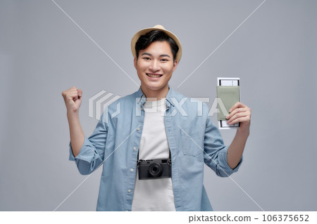 Man feeling happy about summer trip, holding passport with plane tickets and backpack, raising hands up in celebration gesture, 106375652