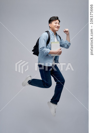 Full length portrait of a smiling young asian man carrying backpack isolated, holding books, jumping 106375666