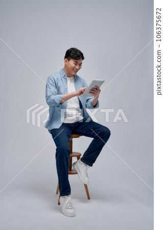 Handsome attractive smiling happy young male using tablet and sitting on the chair Handsome attractive smiling happy young male using tablet and sitting on the chair 106375672