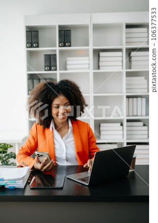 Young African woman typing on tablet and laptop while sitting at the working black table office.. Young African woman typing on tablet and laptop while sitting at the working black table office.. 106377533