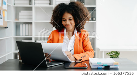 Young African woman typing on tablet and laptop while sitting at the working black table office.. Young African woman typing on tablet and laptop while sitting at the working black table office.. 106377536