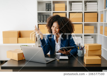 Startup small business SME, Entrepreneur owner African woman using smartphone or tablet taking receive and checking online purchase shopping order to preparing pack product box. . 106377580