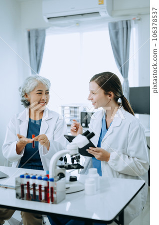 Two scientist or medical technician working, having a medical discuss meeting with an Asian senior female scientist supervisor in the laboratory with online reading, test samples and innovation for Two scientist or medical technician working, having a medical discuss meeting with an Asian senior female scientist supervisor in the laboratory with online reading, test samples and innovation for 106378537