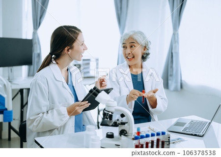 Two scientist or medical technician working, having a medical discuss meeting with an Asian senior female scientist supervisor in the laboratory with online reading, test samples and innovation for Two scientist or medical technician working, having a medical discuss meeting with an Asian senior female scientist supervisor in the laboratory with online reading, test samples and innovation for 106378538