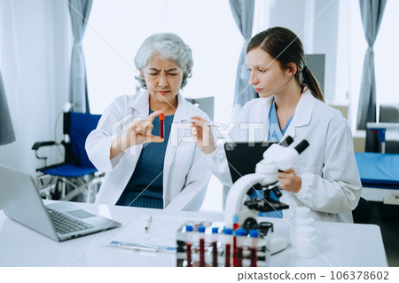 Two scientist or medical technician working, having a medical discuss meeting with an Asian senior female scientist supervisor in the laboratory with online reading, test samples and innovation for Two scientist or medical technician working, having a medical discuss meeting with an Asian senior female scientist supervisor in the laboratory with online reading, test samples and innovation for 106378602