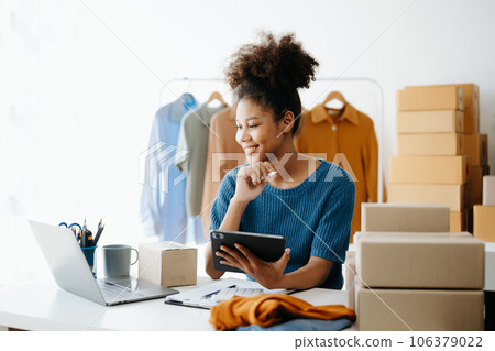 Young African woman running online store Startup small business SME, using smartphone or tablet taking receive and checking online purchase shopping order in office 106379022