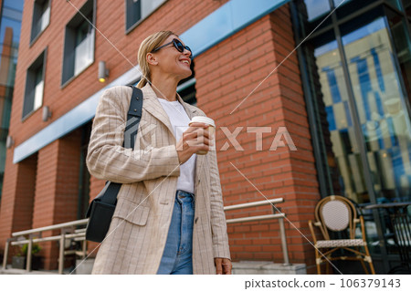 Smiling business woman drinking coffee during break time near office building 106379143