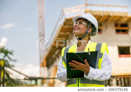 Professional female engineer in protective helmet making notes on construction site 106379186