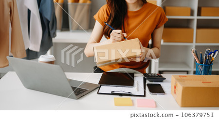 Young woman holding a smartphone, tablet showing payment success and credit card with yellow parcel box as online shopping concept  in home office 106379751