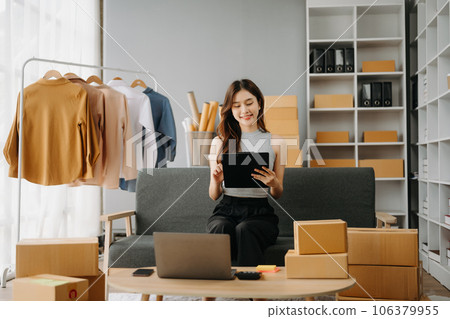 Young Asian business owner woman prepare parcel box and standing check online orders for deliver to customer on tablet, laptop Shopping Online concept.. Young Asian business owner woman prepare parcel box and standing check online orders for deliver to customer on tablet, laptop Shopping Online concept.. 106379955