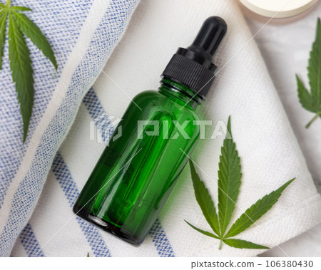 Green glass dropper bottle near green cannabis leaves top view, CBD cosmetic mockup Green glass dropper bottle near green cannabis leaves top view, CBD cosmetic mockup 106380430