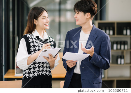 Asian business colleague business presents and explains and using laptop and tablet. Teamwork, financial marketing team, while sitting in modern office room.. 106380711