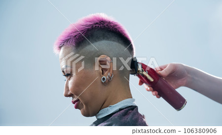 The hairdresser shaves the back of the head of a female client. Rear view of a woman with short pink hair in a barbershop. 106380906