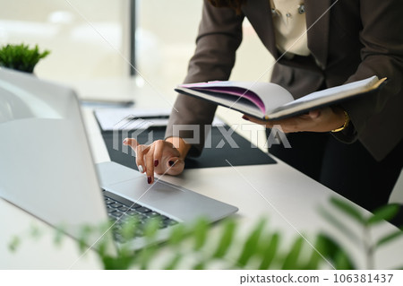 Businesswoman holding notepad and typing on laptop computer. Business, technology and communication Businesswoman holding notepad and typing on laptop computer. Business, technology and communication 106381437