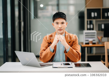 Young attractive Asian male office worker business suits smiling at camera in office Young attractive Asian male office worker business suits smiling at camera in office 106382010