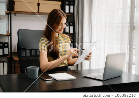 Confident Asian woman with a smile standing holding notepad and tablet at the home office.. Confident Asian woman with a smile standing holding notepad and tablet at the home office.. 106382218